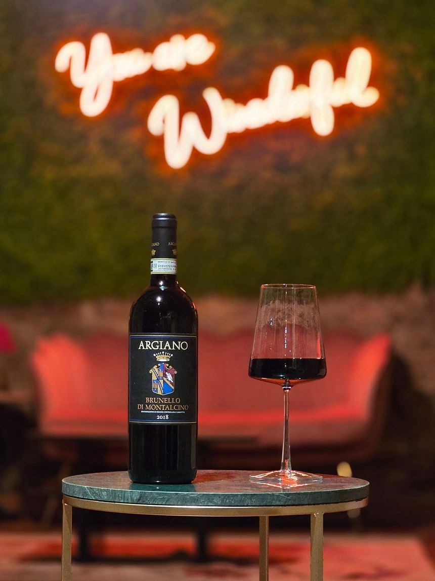 Bottiglia di Brunello di Montalcino Argiano 2018 su un tavolino di marmo verde, sullo sfondo l'angolo lounge