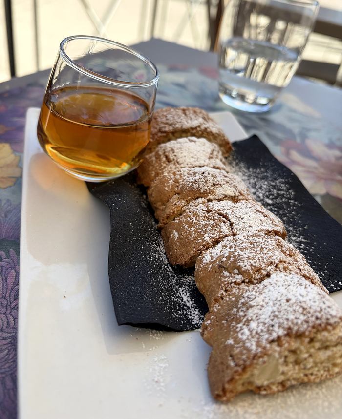 Cantucci serviti con un bicchierino di Vin Santo su un tavolo alla luce del giorno