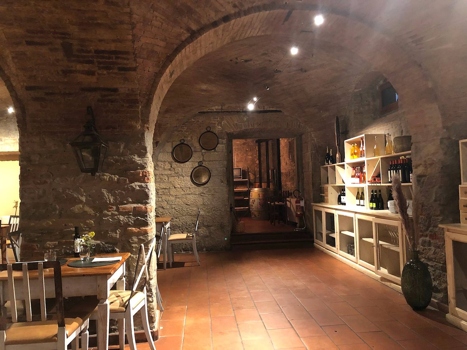 La sala di Quanto Basta sotto la volta in mattoni, con i muri in pietra, il pavimento in cotto e la cantina in fondo