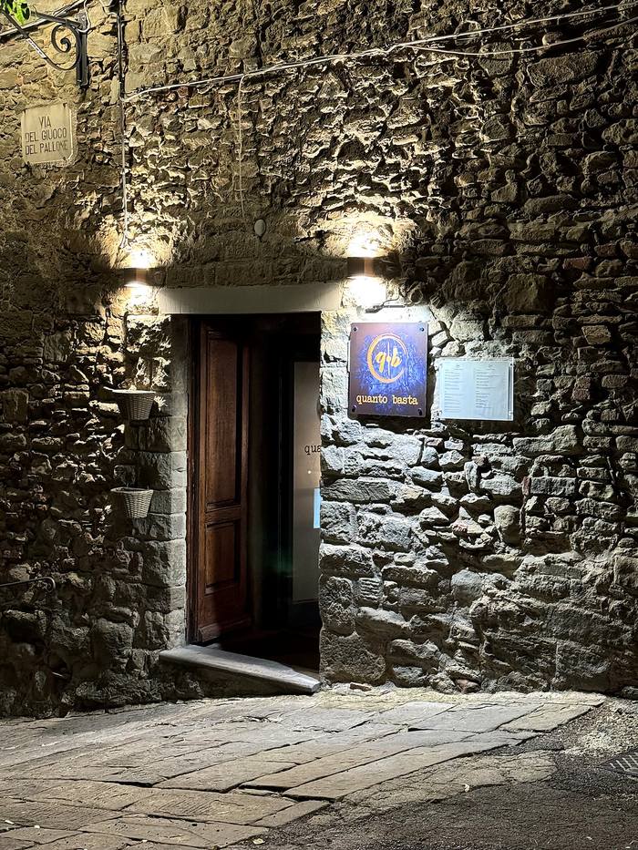 L'ingresso di sera: insegna arancione su fondo blu scuro, il menù esposto e la targa della via
