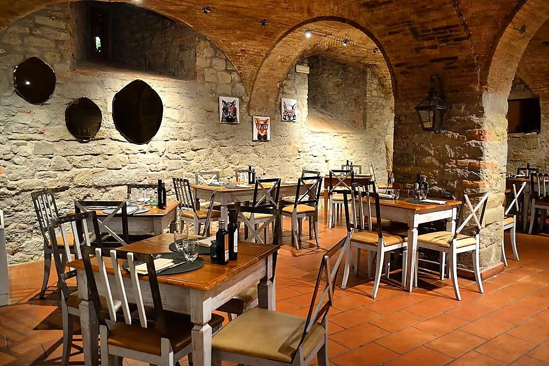 La sala di Quanto Basta vista in lunghezza: una fila di archi in mattoni, tavoli apparecchiati e sedie in legno chiaro