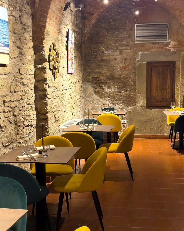 La sala la sera: sedie imbottite senape e verde petrolio, dischi di rame alle pareti, lampade da tavolo in ottone