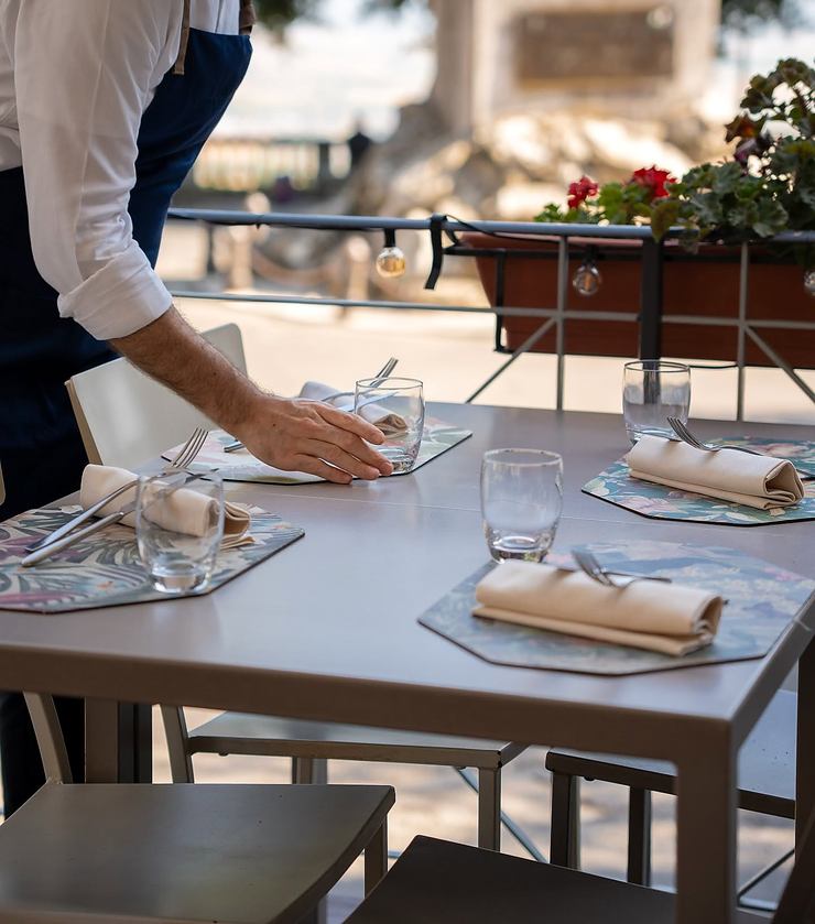 Un cameriere con grembiule blu apparecchia un tavolo sulla terrazza